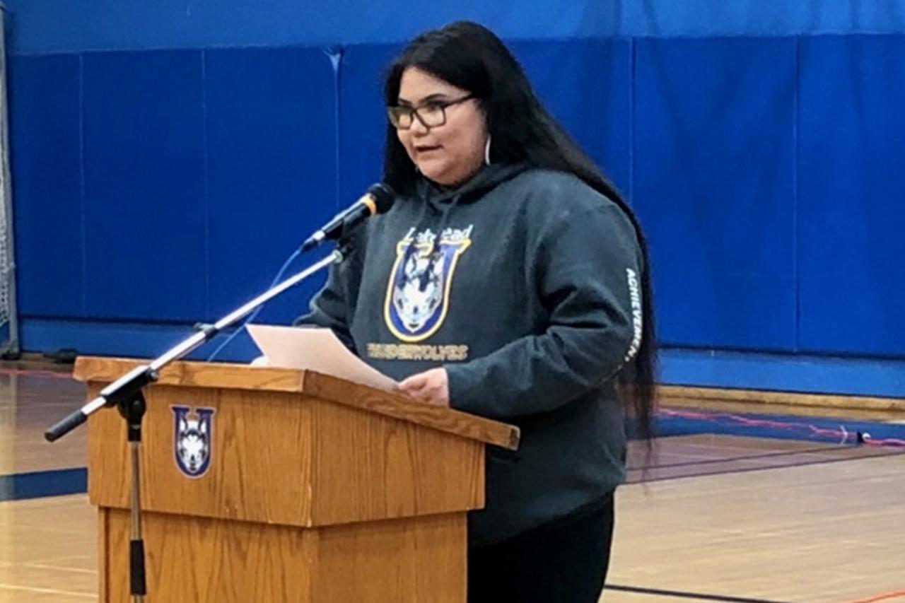 Lakeishia Meekis, standing at a Lakehead University podium wearing a gray Lakehead Thunderwolves sweater. She is an Achievement Program alum who encouraged the students to continue to push themselves.